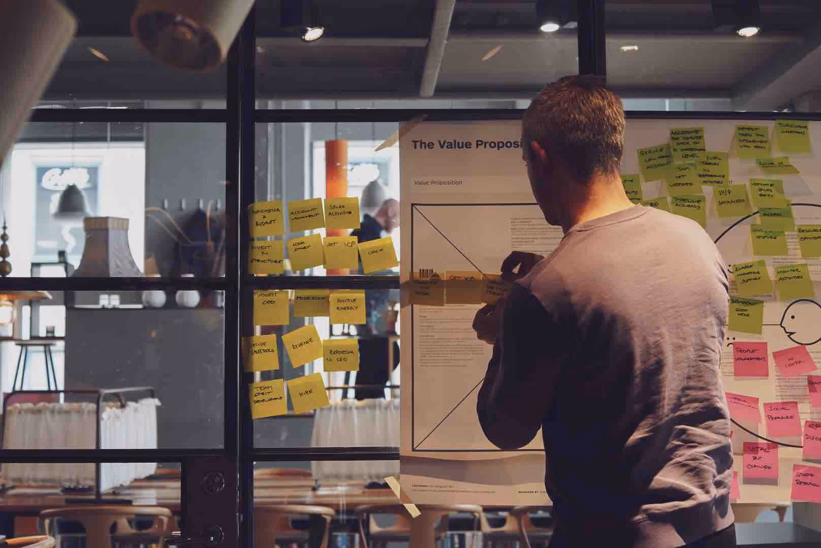 A person at a wall of sticky notes under a printed value proposition canvas
